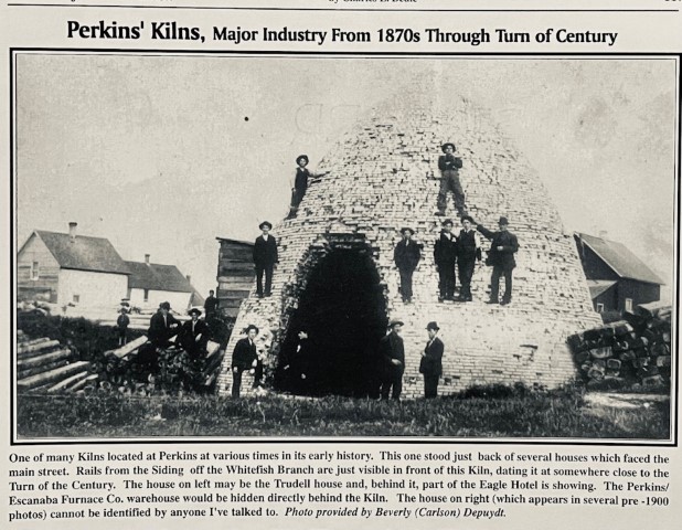 Perkins' Kilns, Major industry from 1870s through turn of Century. One of many kilns located at Perkins at various times in its early history. This one stood just back of several houses which faced the main street. Rails from the Siding off the Whitefish Branch are just visible in front of this Kiln, dating it at somewhere close to the Turn of the Century. The house on left may be the Trudell house and, behind it, part of the Eagle Hotel is showing. The Perkins/Escanaba Furnace Co. warehouse would be hidden directly behind the Kiln. The house on right (which appears in several pre-1900 photos) cannot be identified by anyone I've talked to. Photo provided by Beverly (Carlson) Depuydt.
